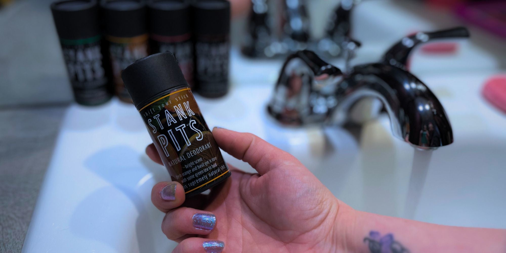 Person with tattoos and painted nails holding plastic-free natural deodorant called Stank Pits.