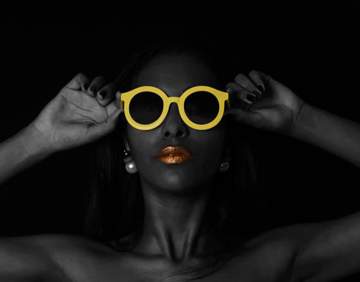 Summer skincare image showing a fabulous Black woman putting on yellow sunglasses.