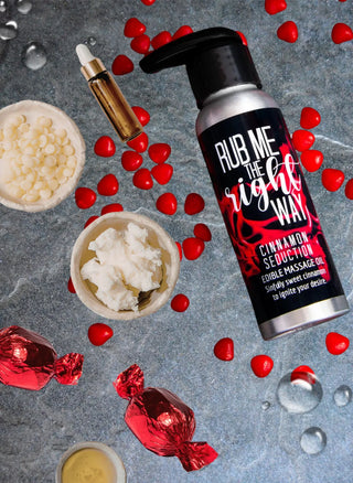 This cinnamon flavored edible massage oil is shown on a gray background with the natural ingredients it's made of in this photo by Badgerface Beauty Supply.